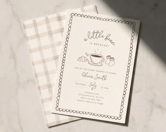May include: A baby shower invitation with the text "a little bean is brewing!" in a whimsical font. The invitation features a coffee cup, croissant, and baby socks illustration. The envelope has a tan and white plaid pattern.