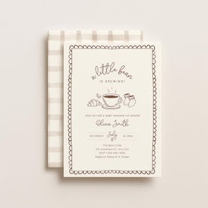 May include: Cream-colored baby shower invitation with a scalloped border and a beige plaid envelope. The invitation features the text "a little bean is brewing!" and includes illustrations of a croissant, coffee cup, and baby socks.