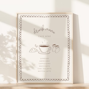 Könnte beinhalten: Ein gerahmter Druck mit einer Getränkekarte für "Café Bébé". Das Design umfasst eine Kaffeetasse, ein Croissant, Babysocken und einen dekorativen Rahmen. Die Speisekarte listet Espresso, Americano, Cappuccino, Macchiato, Chai Tea Latte und Matcha Latte auf.