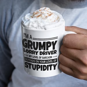 May include: White ceramic mug with the text "I'M A GRUMPY LORRY DRIVER *** MY LEVEL OF SARCASM *** DEPENDS ON YOUR LEVEL OF STUPIDITY". The mug is filled with a white beverage and topped with whipped cream and a sprinkle of cinnamon.
