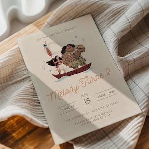 May include: A light beige invitation card with the text "Melody Turns 2" and a cartoon illustration of characters in a boat. The card includes event details: date, time, and RSVP information. The card is resting on a white and beige fabric.