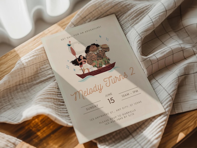 May include: A light beige invitation card with the text "Melody Turns 2" and a cartoon illustration of characters in a boat. The card includes event details: date, time, and RSVP information. The card is resting on a white and beige fabric.