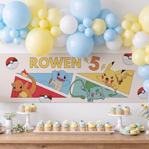 May include: A rectangular banner featuring the text ROWEN 5 and illustrations of Charmander, Squirtle, Bulbasaur, and Pikachu, surrounded by a balloon arch in light blue, yellow, and white, displayed above a table with cupcakes and macarons.