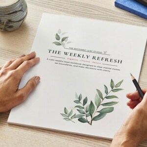 May include: A white workbook titled "THE WEEKLY REFRESH" with green leaf illustrations. The text reads "A calm weekly reset workbook designed to clear mental clutter, set boundaries, and make decisions with clarity." A pencil rests on the page.