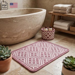 May include: A mauve and white geometric patterned bath mat, handmade and rectangular, sits on a tiled bathroom floor. A matching basket and potted succulents are also visible. The image includes a PDF pattern icon.