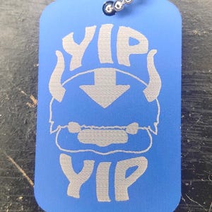 May include: Blue dog tag with the word "YIP" above and below a stylized character with an arrow. The tag is attached to a metal ball chain.