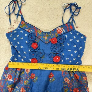 May include: Blue floral top with crocheted red and blue flowers. The top has adjustable tie straps and a V-neckline. The bottom of the top has a floral pattern. The text on the ruler says "A Touch of KLAFF'S".