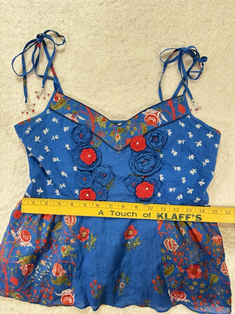 May include: Blue floral top with crocheted red and blue flowers. The top has adjustable tie straps and a V-neckline. The bottom of the top has a floral pattern. The text on the ruler says "A Touch of KLAFF'S".