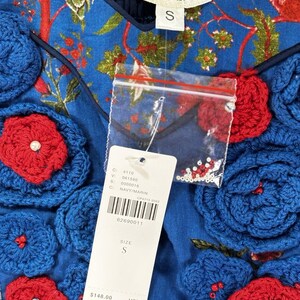 May include: Blue top with red and blue floral crochet details. The top has a V-neck and a tag that reads "NIKAHA" and "S". The top has a floral pattern and a price tag.