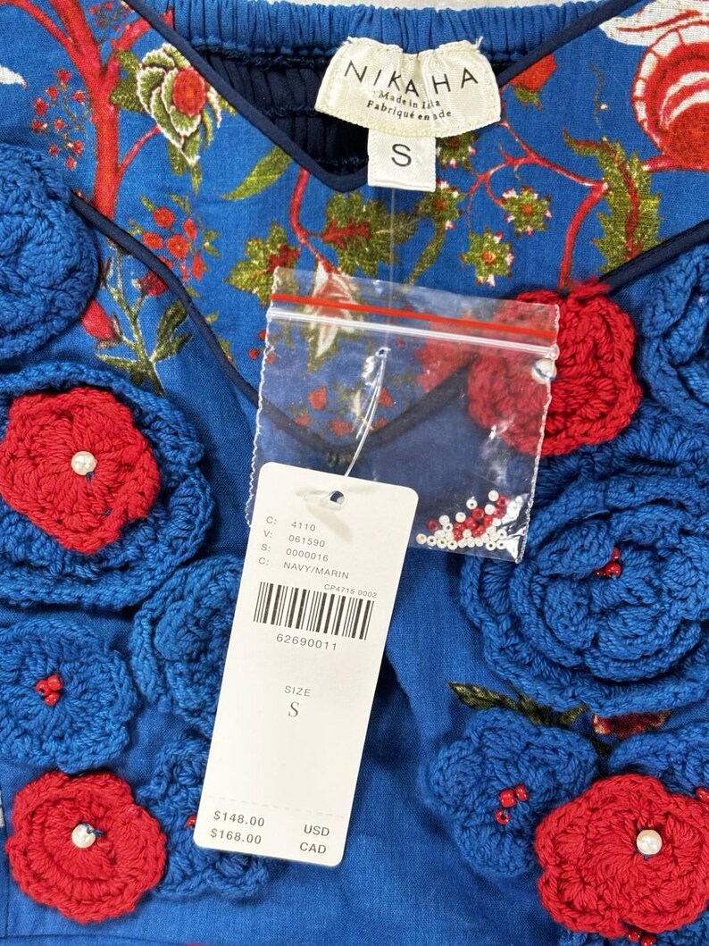 May include: Blue top with red and blue floral crochet details. The top has a V-neck and a tag that reads "NIKAHA" and "S". The top has a floral pattern and a price tag.