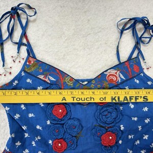 May include: Blue floral print top with red and blue crochet flower accents. The top has tie straps and a decorative floral trim. The text "A Touch of KLAFF'S" is visible on a yellow ruler.