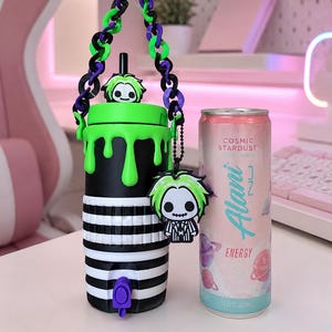 May include: A black and white striped tumbler with a bright green drip lid, a purple and green chain handle, and a character charm. The tumbler features a purple spout and is positioned next to a 12 fluid ounce Cosmic Stardust Alani Nu energy drink can.
