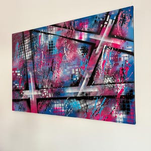 Puede incluir: Obra de arte abstracta con una vibrante mezcla de colores. La obra presenta un diseño geométrico azul, rosa y negro con salpicaduras de pintura blanca y negra. La pieza está firmada en la esquina inferior izquierda.