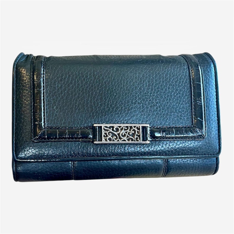 May include: Black leather wallet with a textured finish. The wallet features a silver-tone decorative clasp with an ornate design. The edges have a glossy, crocodile-like texture.