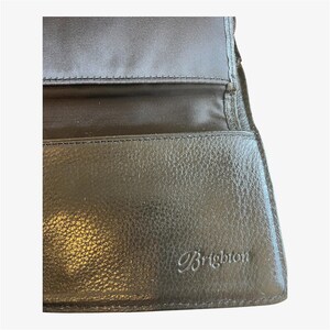 May include: Black leather wallet with the embossed brand name "Brighton". The wallet is open, revealing a black fabric lining and multiple compartments. The leather has a textured appearance.