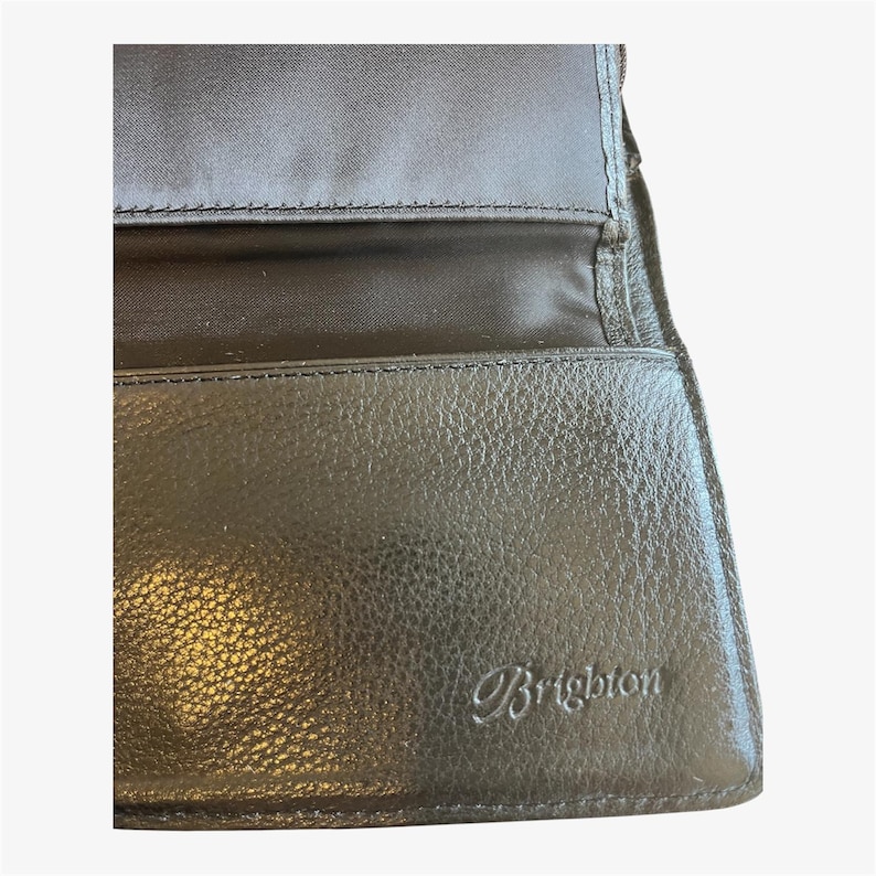 May include: Black leather wallet with the embossed brand name "Brighton". The wallet is open, revealing a black fabric lining and multiple compartments. The leather has a textured appearance.
