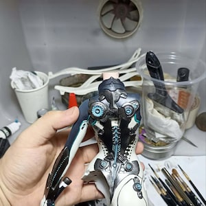 K&ouml;nnte beinhalten: Ein teilweise zusammengebauter Figuren-Torso mit einem komplexen mechanischen Design in den Farben Wei&szlig;, Schwarz und Dunkelblau. Das St&uuml;ck enth&auml;lt komplizierte kreisf&ouml;rmige Details, blaue Akzente und eine segmentierte Wirbels&auml;ulenstruktur.