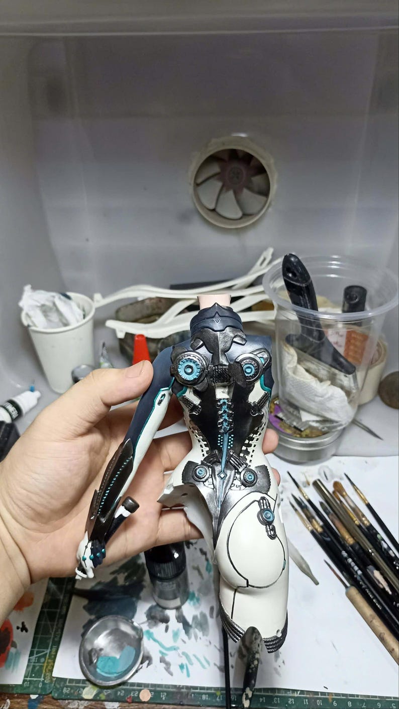 K&ouml;nnte beinhalten: Ein teilweise zusammengebauter Figuren-Torso mit einem komplexen mechanischen Design in den Farben Wei&szlig;, Schwarz und Dunkelblau. Das St&uuml;ck enth&auml;lt komplizierte kreisf&ouml;rmige Details, blaue Akzente und eine segmentierte Wirbels&auml;ulenstruktur.