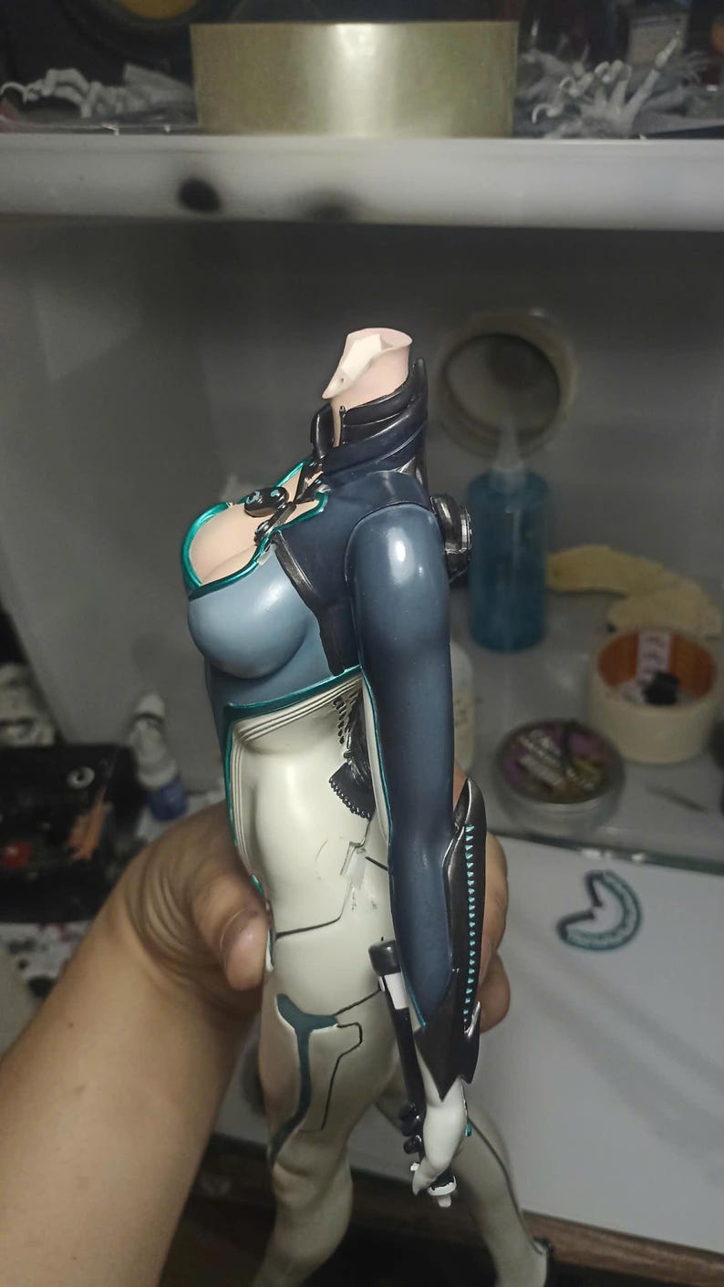 K&ouml;nnte beinhalten: Ein kopfloser Actionfiguren-Torso in einem dunkelblauen und wei&szlig;en Anzug mit t&uuml;rkisfarbenen Akzenten. Die Figur hat einen hohen Kragen, ein eng anliegendes Oberteil und lange &Auml;rmel mit schwarzen Unterarmsch&uuml;tzern sowie detaillierte Linien.