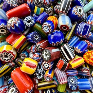 May include: A large collection of multi-colored glass trade beads featuring various shapes and patterns. The beads display intricate designs including chevron, striped, and floral motifs in vibrant shades of blue, red, yellow, white, and black.