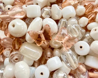 Puede incluir: Un surtido de cuentas de diferentes formas y colores. Las cuentas son principalmente blancas, melocotón y transparentes, con diseños redondos, cuadrados y de mariposa. Ideal para la creación de joyas y manualidades.