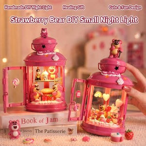 May include: Pink Strawberry Bear DIY small night lights with open doors, featuring bear figurines, strawberries, and candies. The text "Strawberry Bear DIY Small Night Light" is visible. The lights are on top of books that say "Book of Jam" and "The Patisserie".