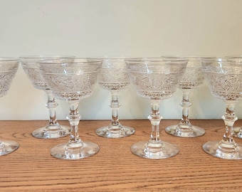 May include: Set of eight clear glass champagne coupes with a delicate etched design. The glasses have a tall, slender stem and a wide, shallow bowl.