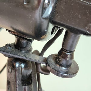 May include: Close-up of a vintage black electric fan. The fan's motor housing and stand are made of dark metal. The image highlights the fan's mechanical details, including the motor housing, blades, and the stand's adjustable features.
