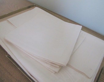 May include: A set of white linen napkins folded and stacked in a box. The napkins are smooth and have a subtle sheen.