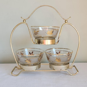 May include: A gold metal serving stand with three glass bowls. The bowls have a frosted glass base with gold leaf accents.
