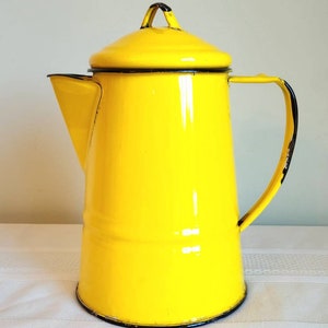 May include: A bright yellow enamel coffee pot with a black rim and handle. The pot has a lid with a black knob.