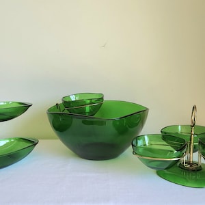 May include: A set of three green glass serving bowls with gold metal stands. The bowls are in different sizes and shapes, and the stands are designed to hold the bowls securely.
