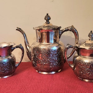 May include: A silver tea set with a teapot, creamer, and sugar bowl. Each piece features an ornate floral design.