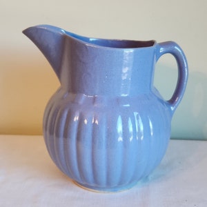 May include: A light blue ceramic pitcher with a ribbed design. The pitcher has a rounded body and a handle.