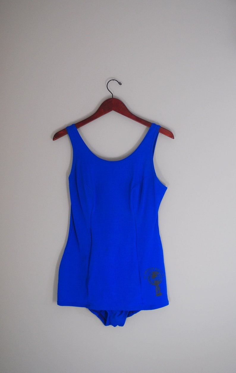 May include: A royal blue one-piece swimsuit with a small graphic on the bottom right side.