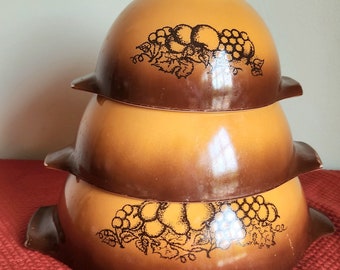 May include: A set of three brown and white mixing bowls with a grape design. The bowls are stacked on top of each other.