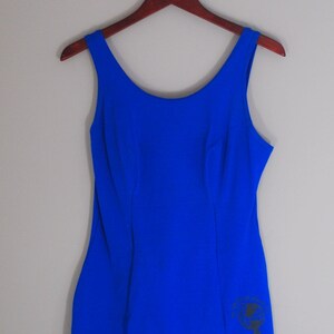 May include: A royal blue one-piece swimsuit with a black graphic on the right side.