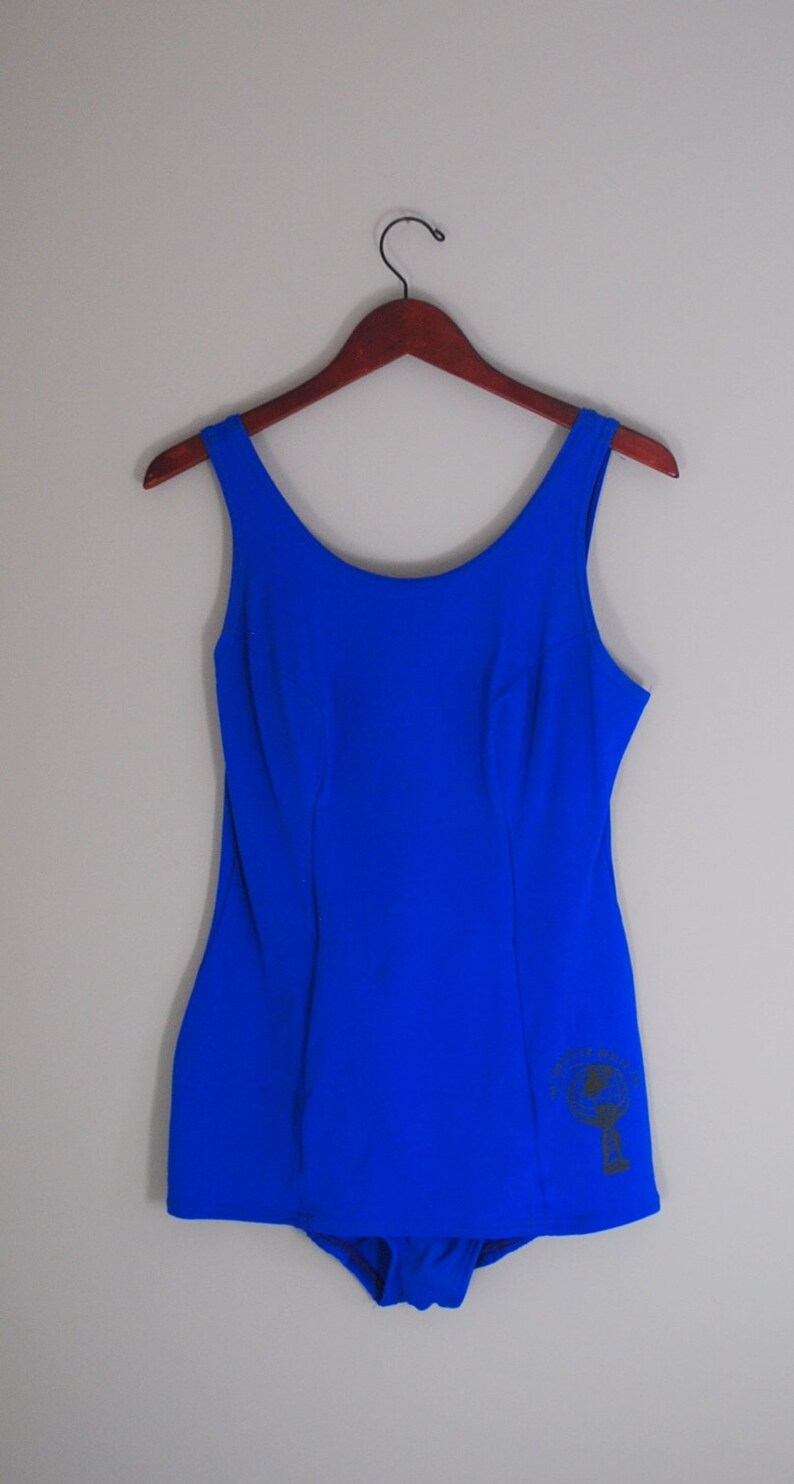 May include: A royal blue one-piece swimsuit with a black graphic on the right side.