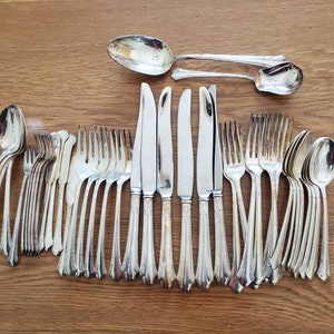 May include: A set of silver flatware, including forks, knives, and spoons, arranged in a row on a wooden surface. The flatware has a traditional design with ornate handles.