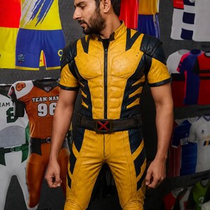 Puede incluir: Un mono de cuero amarillo y negro que presenta una parte superior de manga corta con cremallera frontal, cuello alto y un cintur&oacute;n en la cintura con un emblema de X roja. La prenda incluye paneles texturizados en los hombros y rodillas reforzadas.