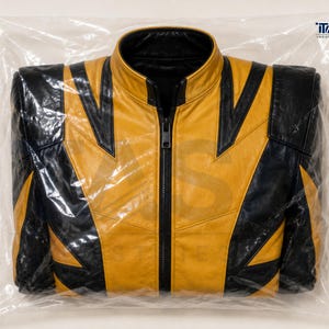 Puede incluir: Una chaqueta de cuero amarilla y negra con cuello alto y cierre de cremallera central negro. La chaqueta presenta un patr&oacute;n geom&eacute;trico de bloques de color con paneles negros sobre los hombros y el pecho. El texto ITASA INDUSTRIES LTD es visible.