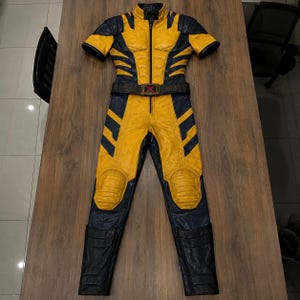 Puede incluir: Un mono de manga corta con un dise&ntilde;o de colores amarillo vibrante y azul marino oscuro con acabado texturizado. La prenda incluye una cremallera frontal central, un cintur&oacute;n con un emblema de X roja y refuerzos acolchados en las rodillas.