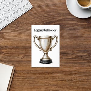 May include: A white card with the text "Legend behavior." features a watercolour illustration of a silver trophy with two handles and a black base. The card is on a wooden surface.