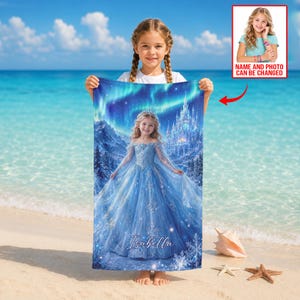 Op de afbeelding: Een gepersonaliseerde strandlaken met een jong meisje in een blauwe jurk, een kasteel en een noorderlicht achtergrond. De handdoek heeft de naam "Isabella" erop gedrukt. Een kleine foto met de tekst "NAME AND PHOTO CAN BE CHANGED" staat rechtsboven.