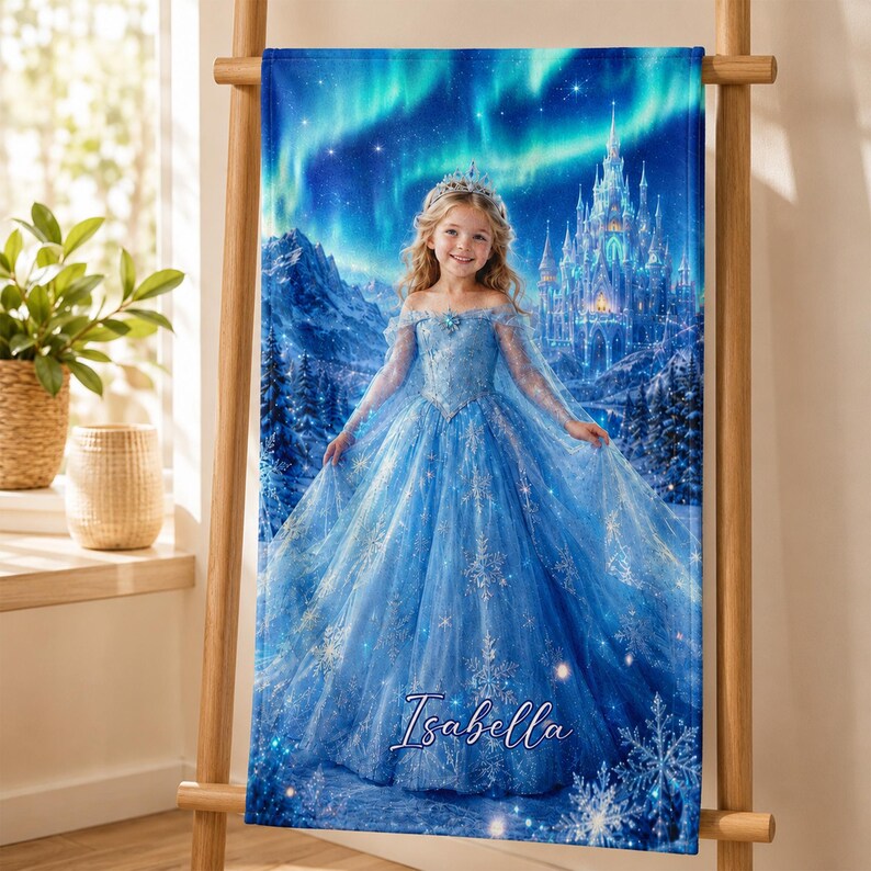 Op de afbeelding: Een blauwe strandlaken met een jong meisje in een blauwe jurk, een tiara en een kasteel in een winterlandschap. De achtergrond toont het noorderlicht. De naam "Isabella" staat onderaan in cursief.