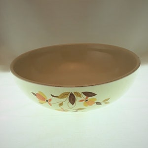 May include: Cream-colored ceramic bowl with a tan interior and floral design. The bowl features a light green exterior with a pattern of orange, yellow, and brown flowers and leaves. The rim has a thin, brown border.