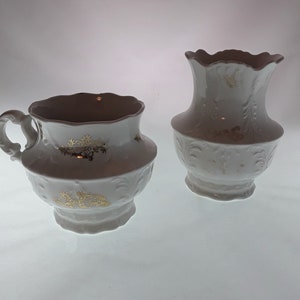 May include: A white porcelain creamer and cup set with gold accents and embossed floral designs.