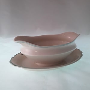 May include: A white porcelain gravy boat with a light blue trim and a matching saucer. The boat has a rounded shape and a spout on one side.