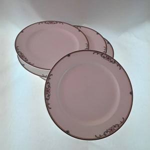 May include: Four pink dinner plates with a floral design and gold trim.