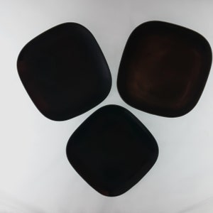 May include: Three black square plates with rounded corners are arranged in a triangular pattern against a white background. The plates have a glossy finish and a simple, modern design, suitable for serving food.